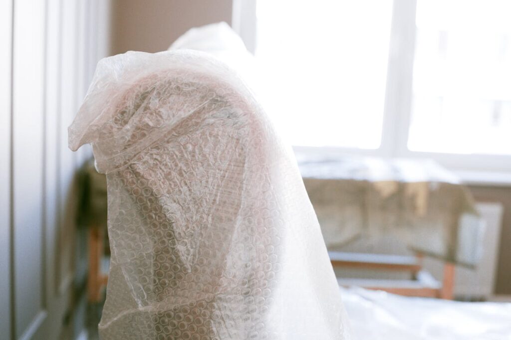 Furniture wrapped in bubble wrap for protection during a move in a bright sunlit room.